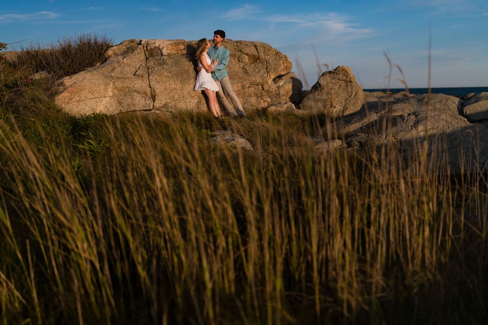 A couple enjoys a scenic overlook on rocky coastal cliffs under bright blue summer skies.