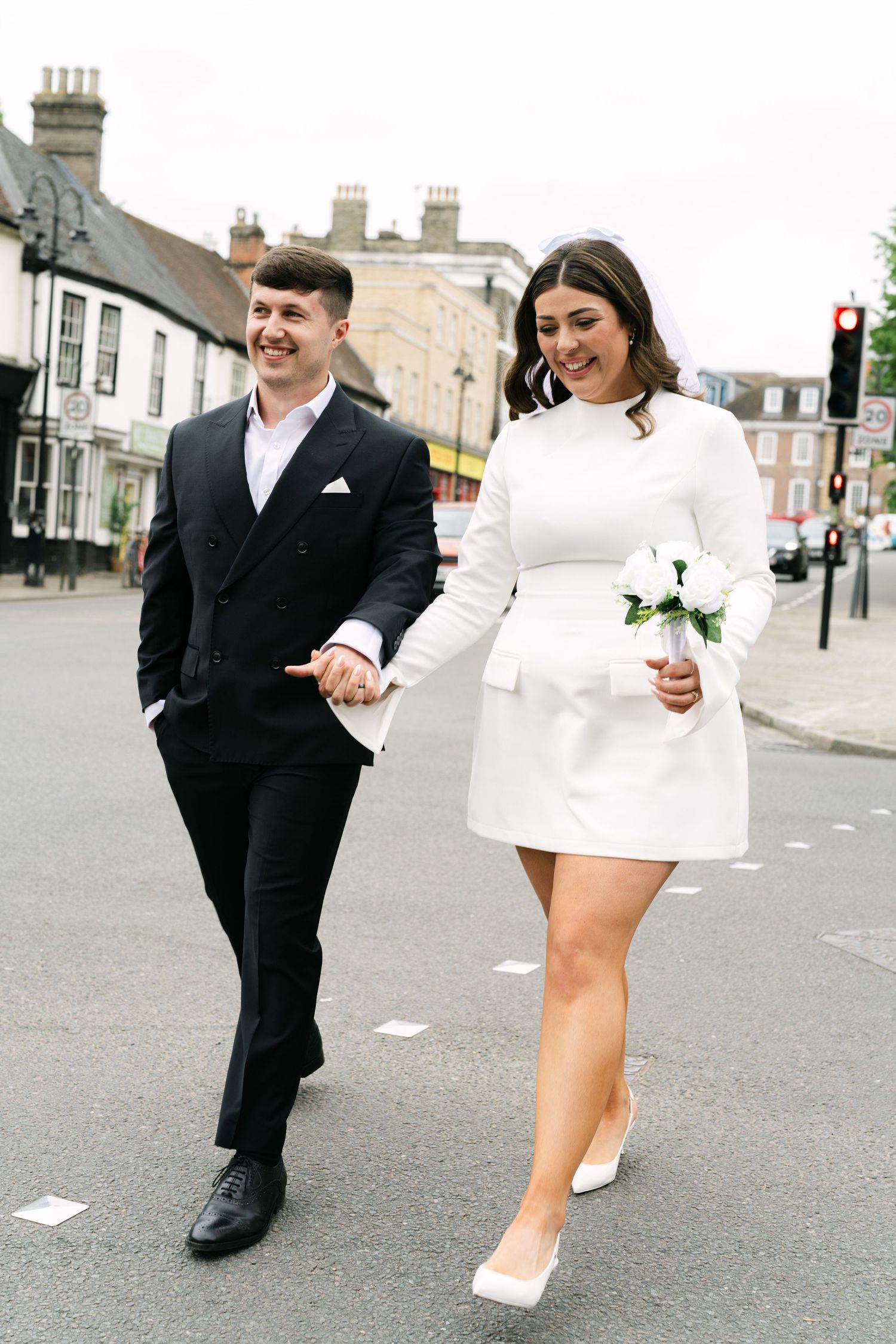 A couple in formal attire walk down a street together while paper pieces fly in the wind in a delightful motion sequence.