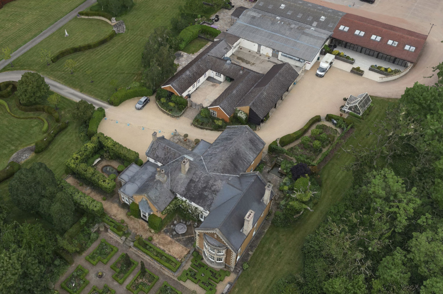 Aerial view of a large country estate with multiple buildings and gray slate roofs surrounded by green landscaping.