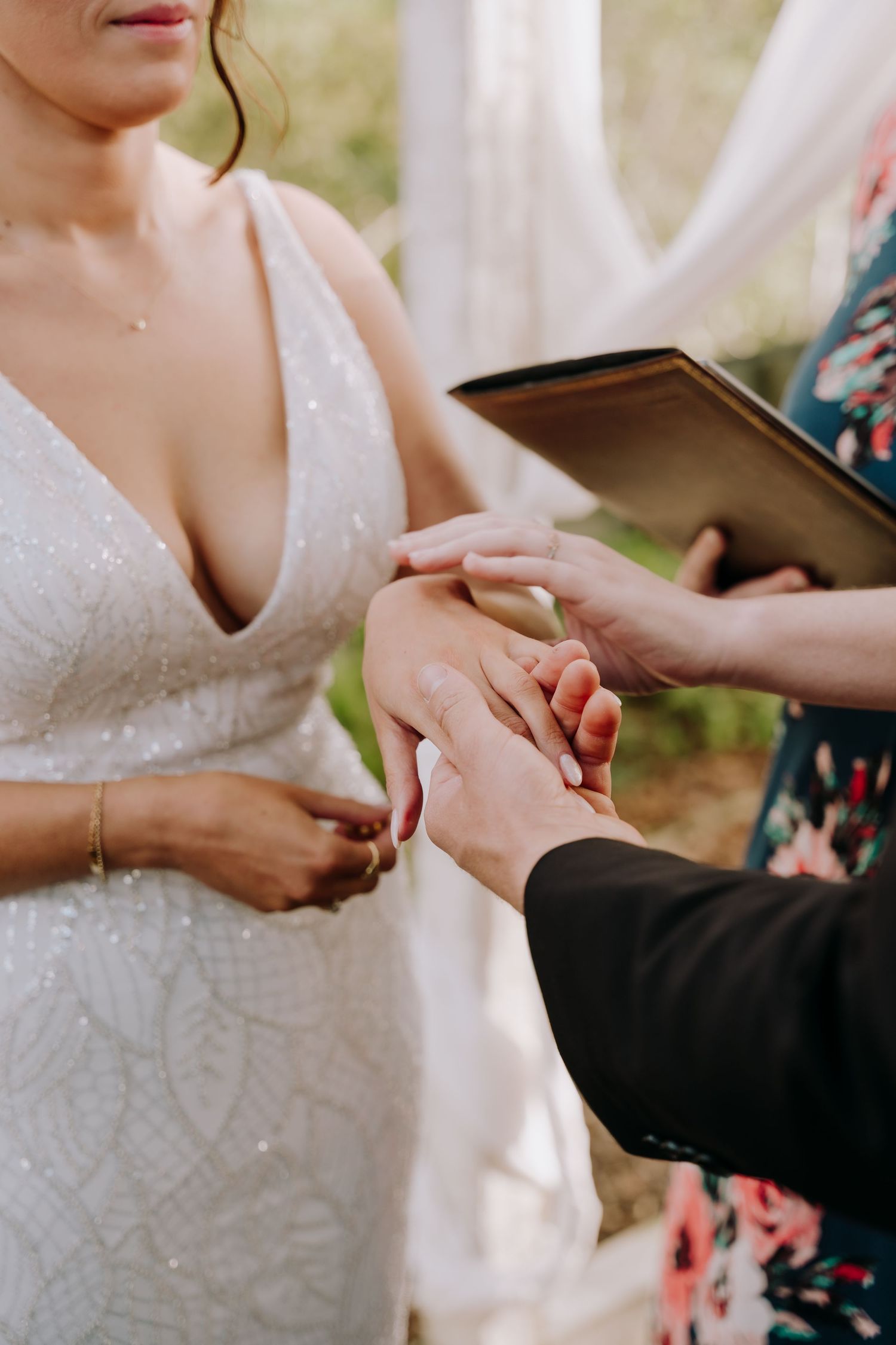 A couple exchanges rings during a wedding ceremony, with the bride wearing a sparkly white lace dress.