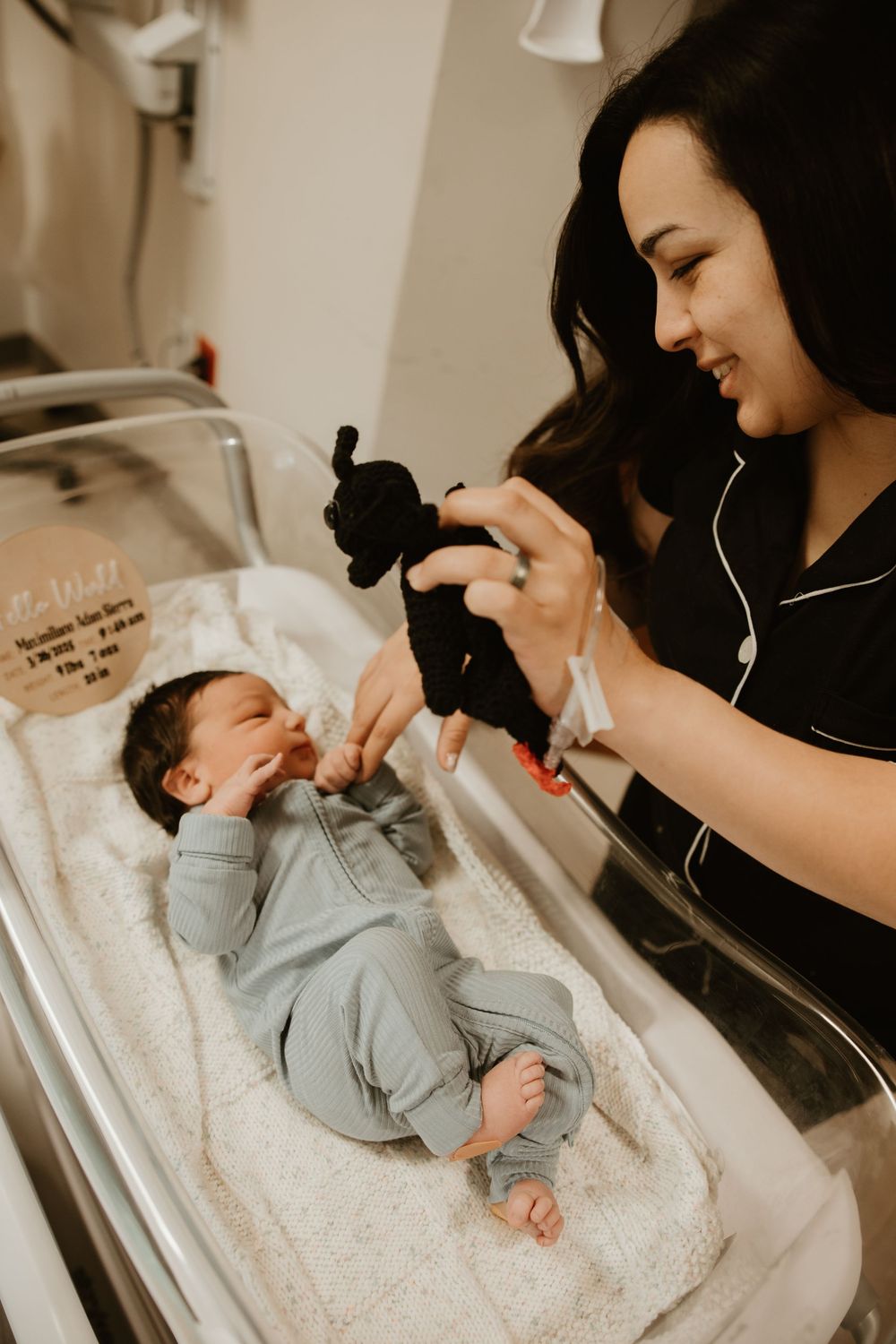 A person in black pajamas plays with a small baby lying on a changing table using a toy puppet to entertain the child.