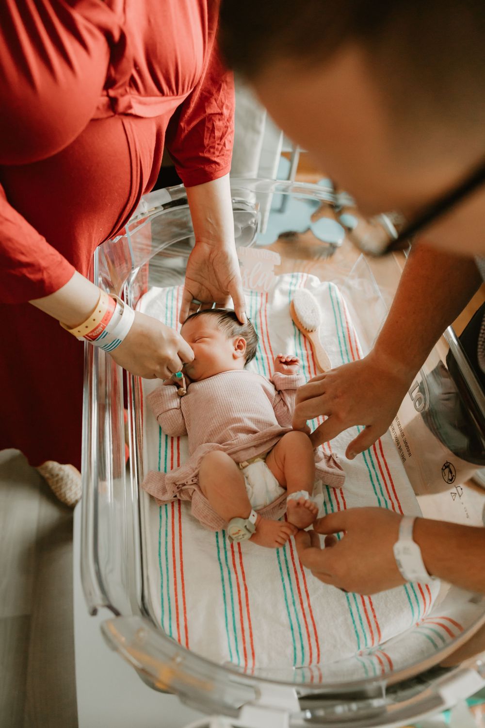 Healthcare providers examine a newborn baby lying on a striped blanket in a hospital bassinet.