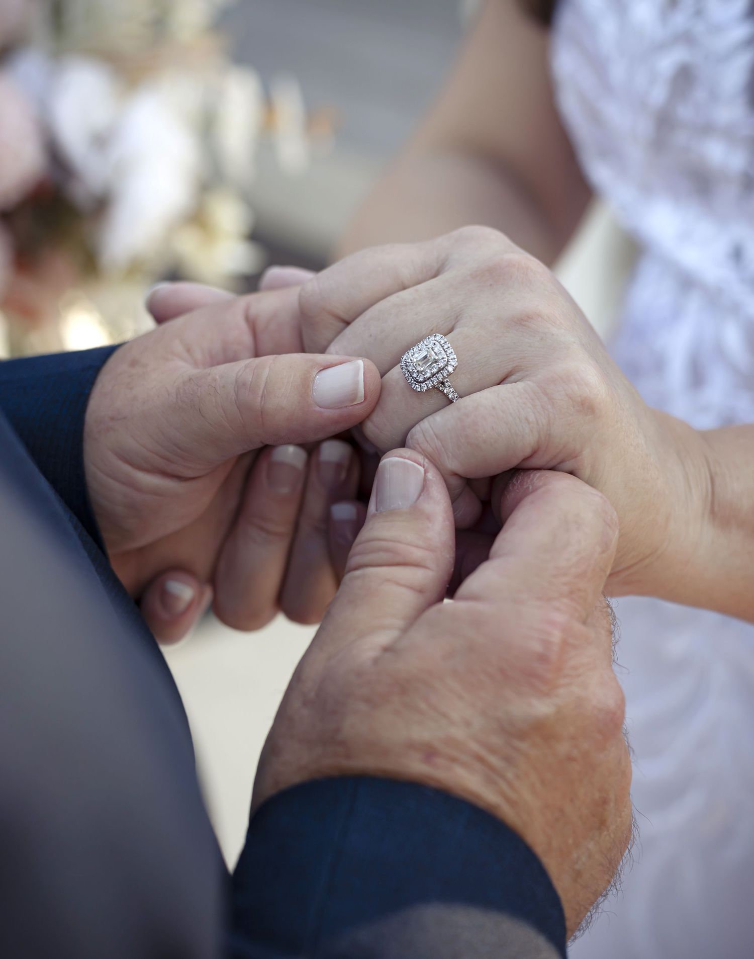 Close-up of hands exchanging a diamond engagement ring during wedding ceremony.