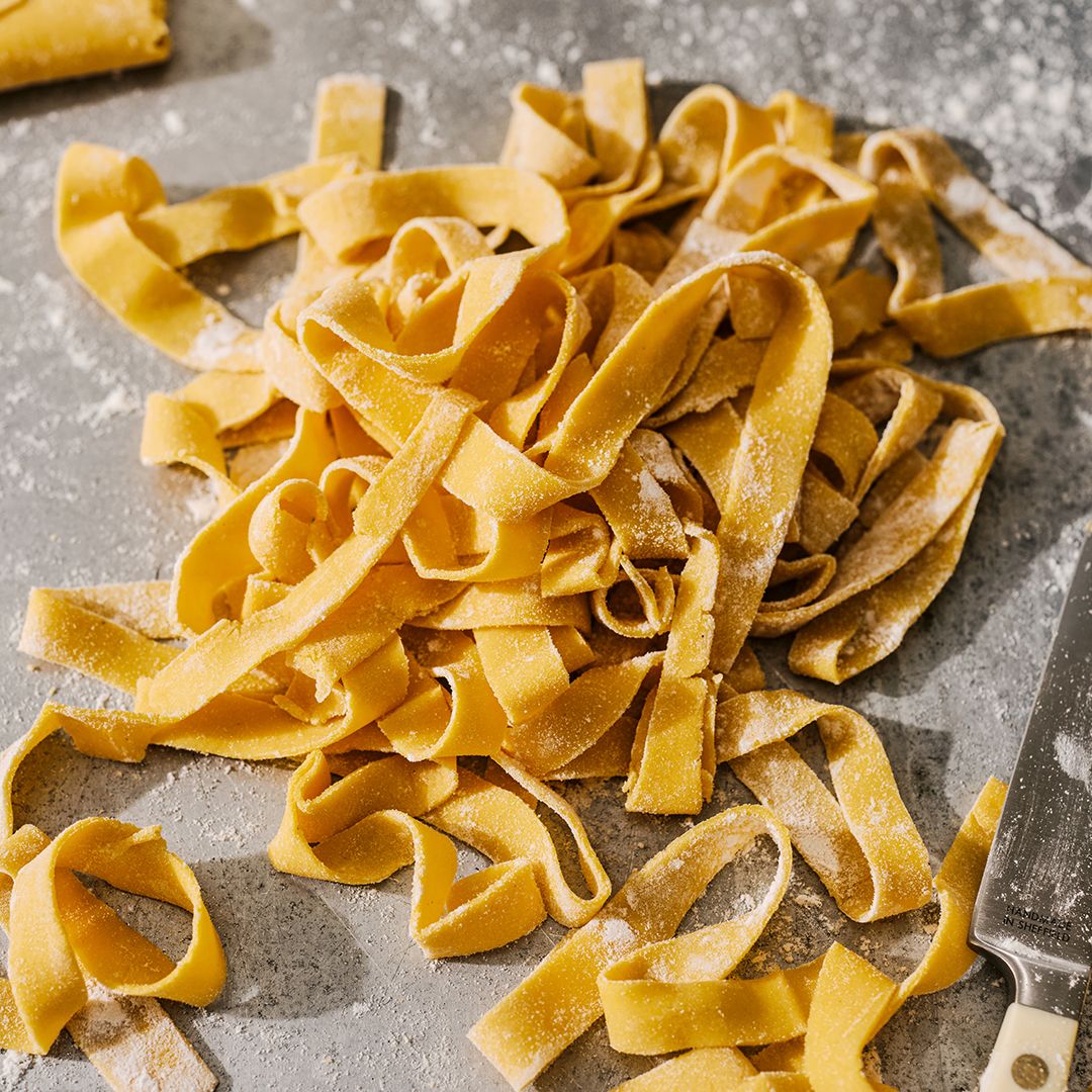 Fresh uncooked pappardelle pasta noodles scattered on a textured grey surface.