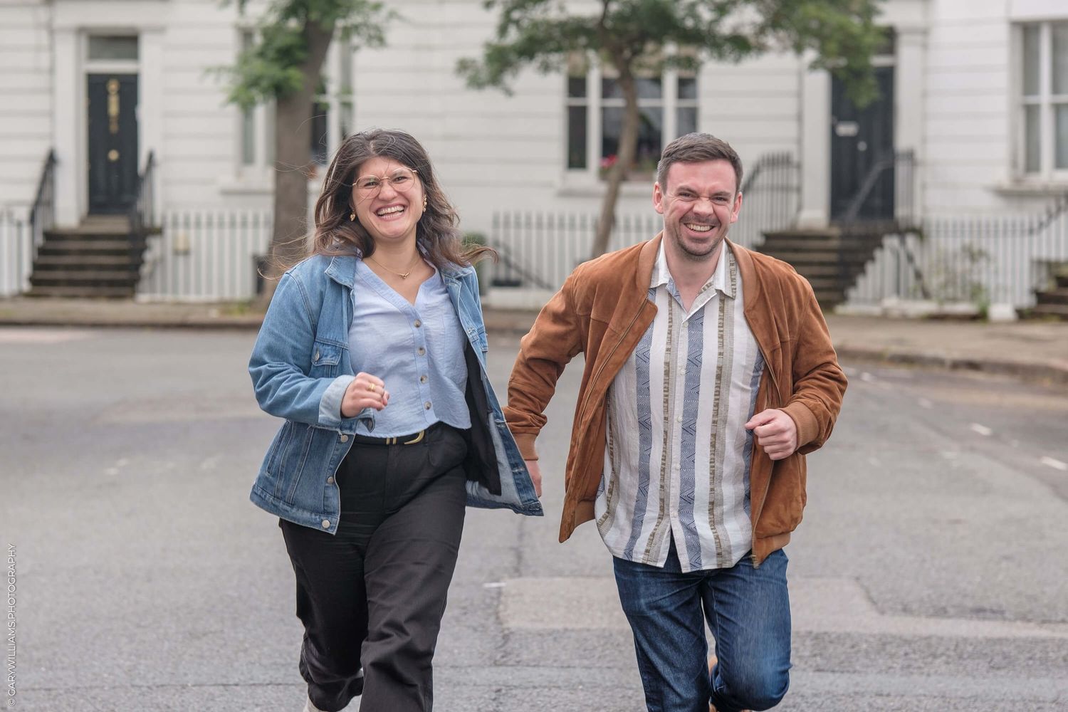 Two people walking together on a residential street wearing casual denim and jackets on a cloudy day.