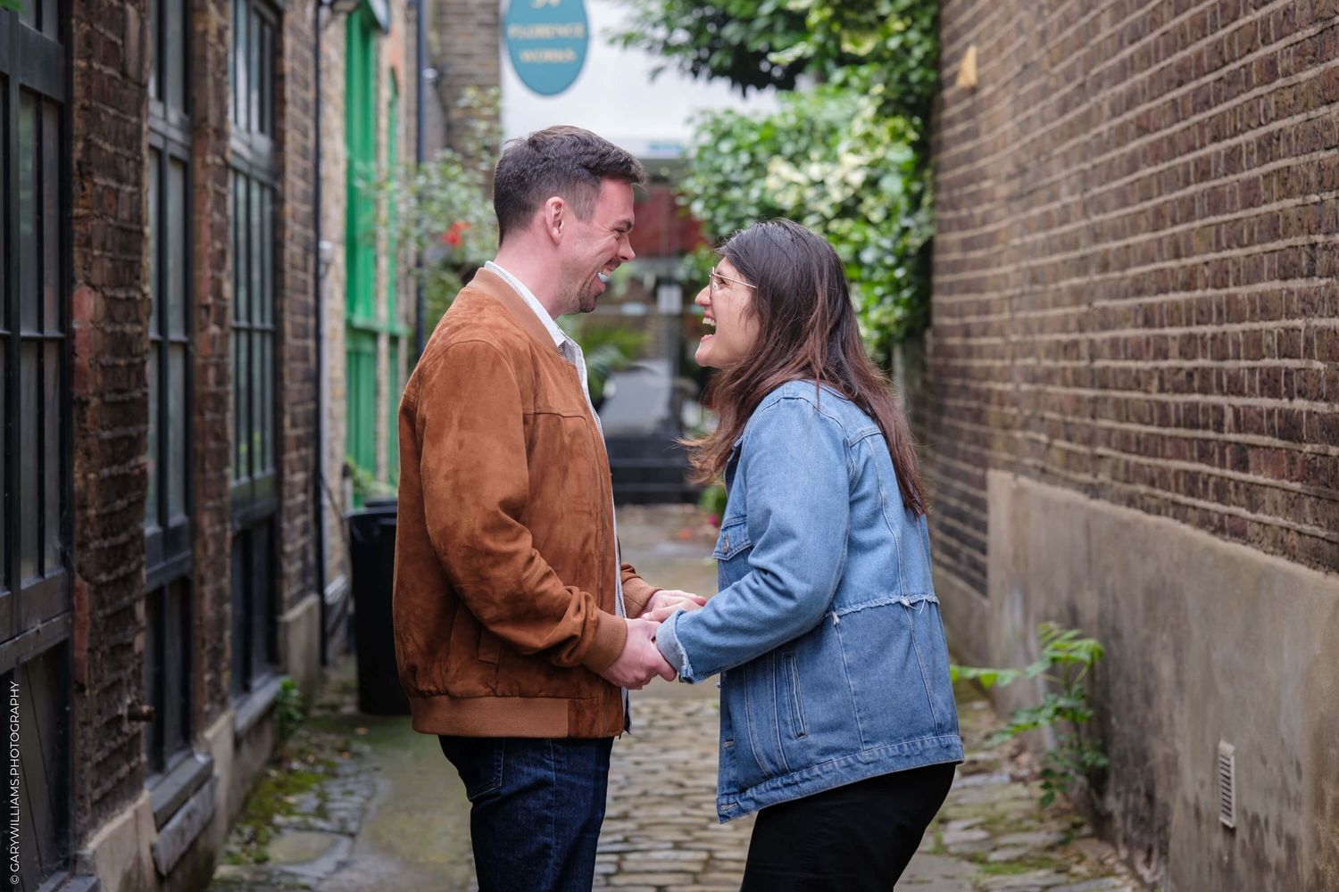 Two people stand close together while facing each other in a narrow brick alleyway.