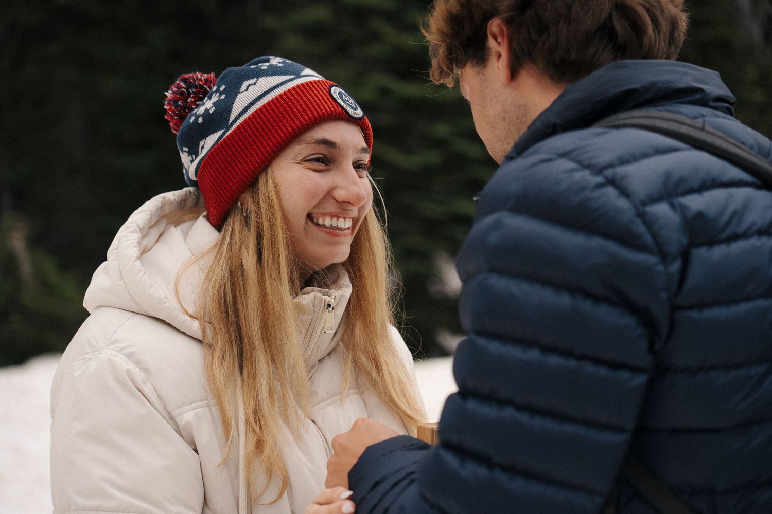 Two people having a joyful conversation while dressed in winter clothing including a knit hat and puffy jackets.