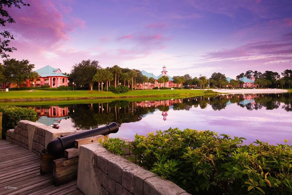 Scenic Disney World's Caribbean Beach Resort with colorful buildings reflecting in calm lake at sunset.