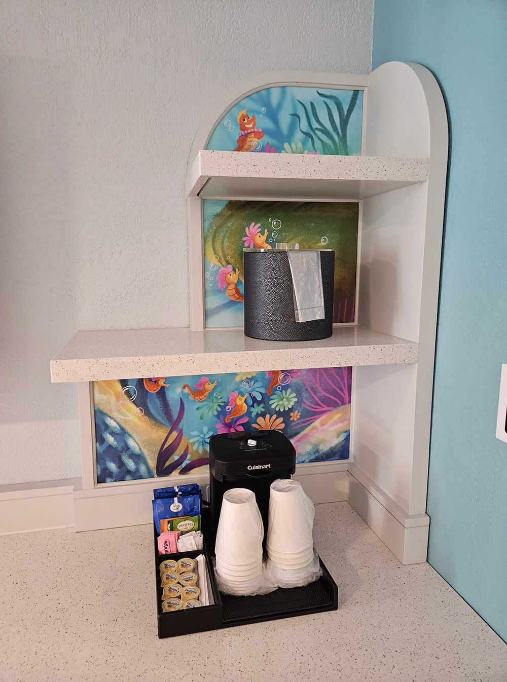 Decorative shelf unit with ocean-themed artwork and hotel amenities.