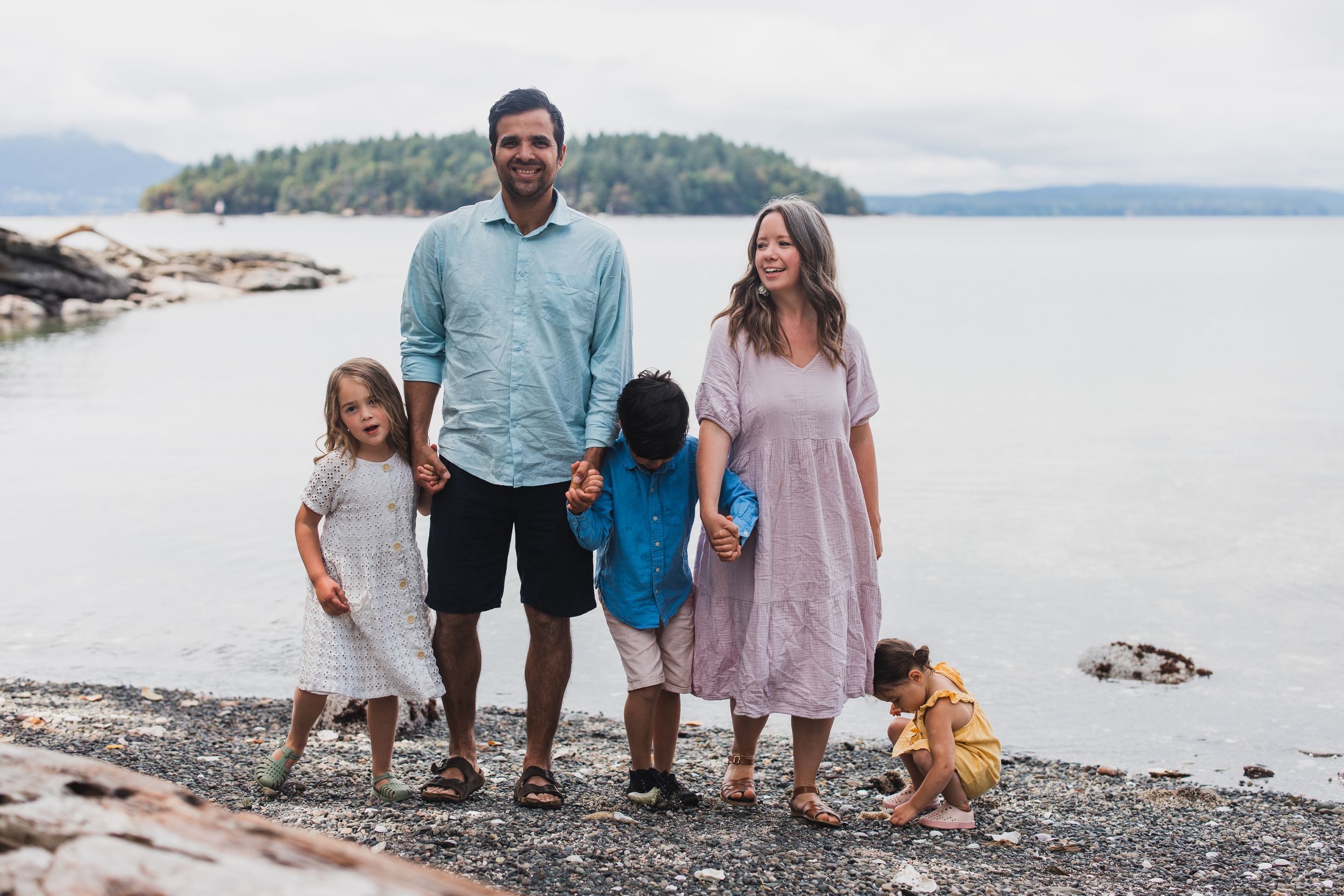 Family enjoying a playful moment together on a rocky beach with water and islands in the background.