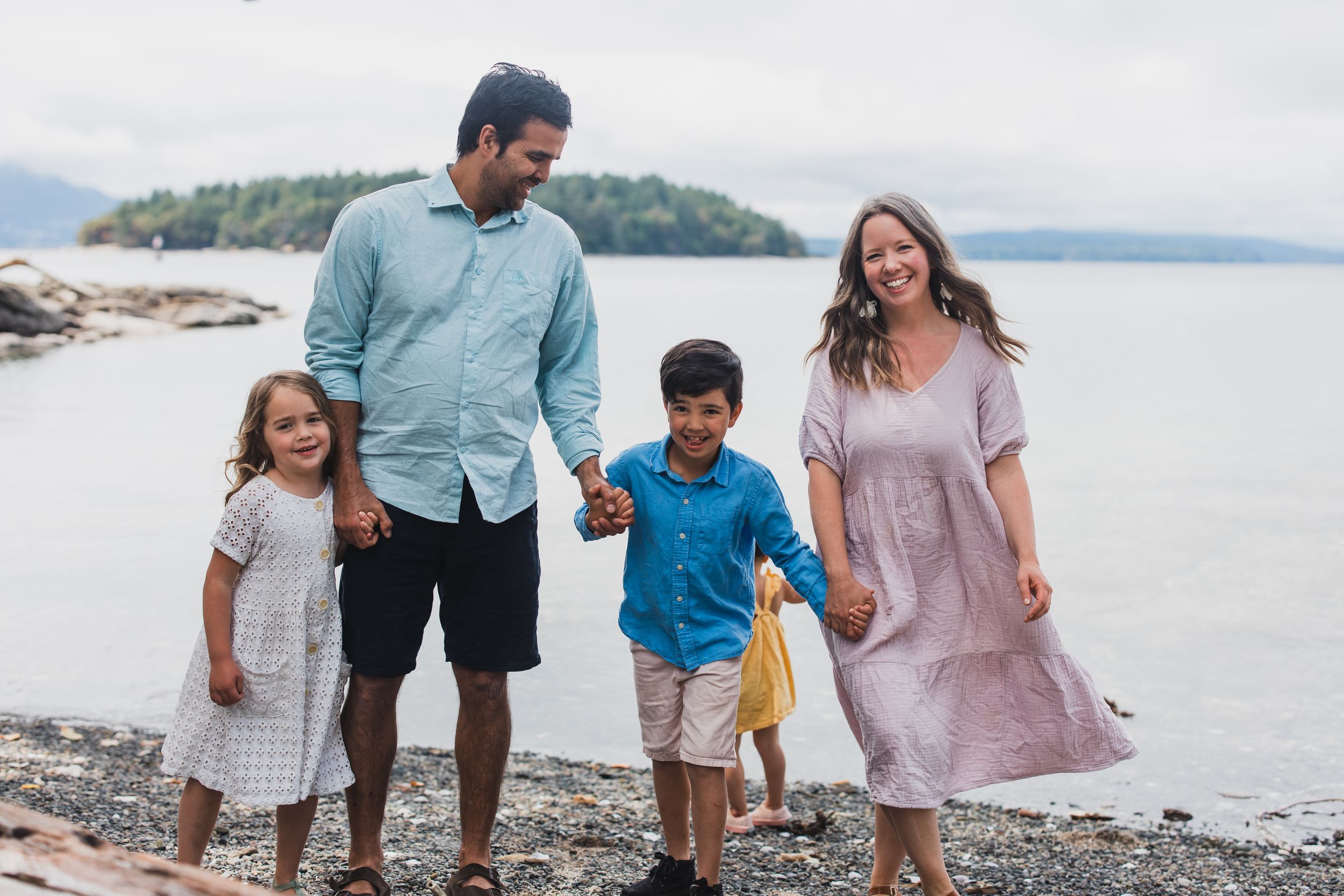 Family wearing coordinated pastel outfits walks along rocky beach shoreline during sunset.