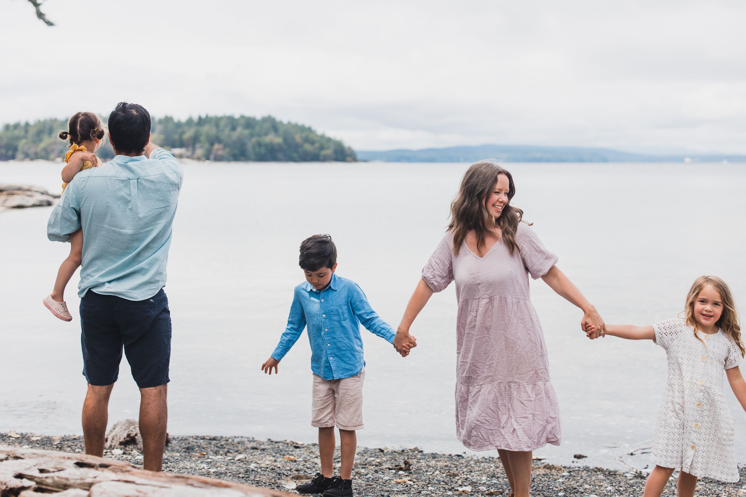 A family enjoys quality time together walking along a rocky beach shoreline with mountains and water in the background.