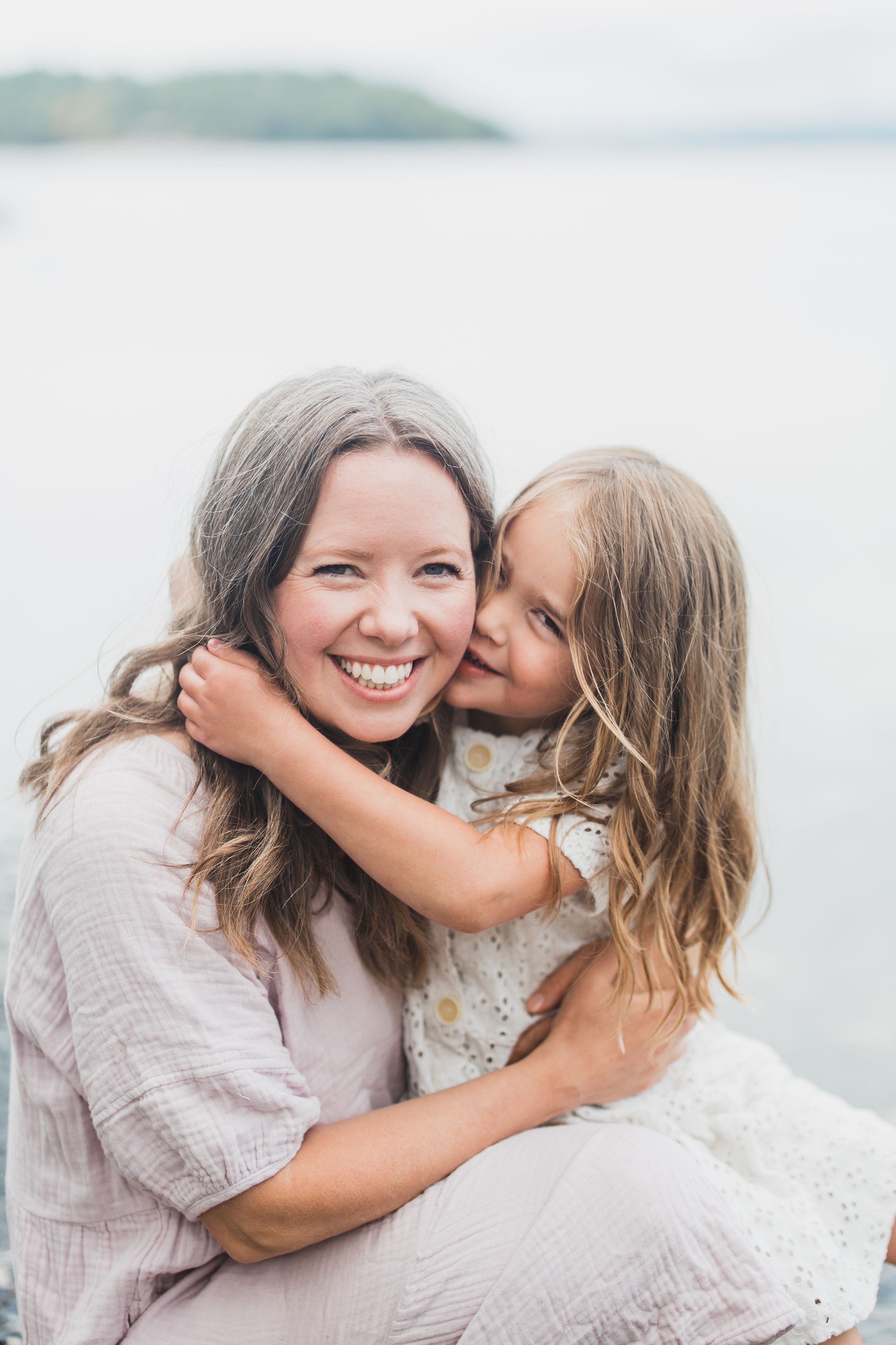 Two people sharing a joyful embrace outdoors with water and mountains in the background.