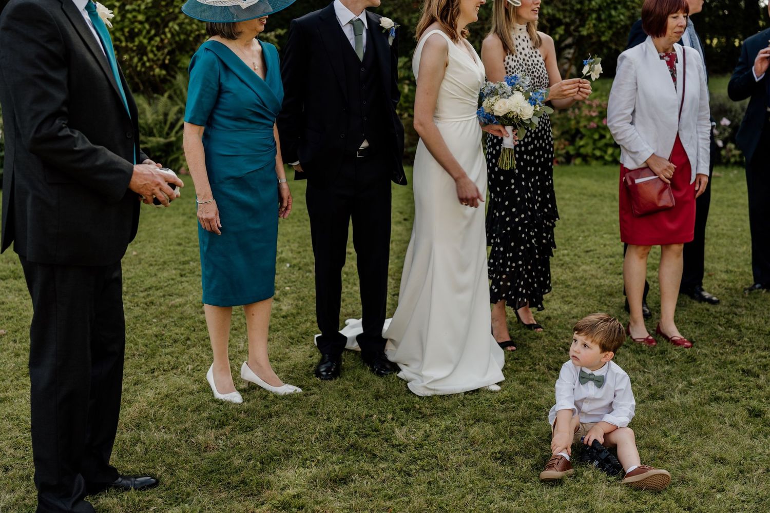 Wedding guests gather on a sunny lawn during an outdoor ceremony reception.