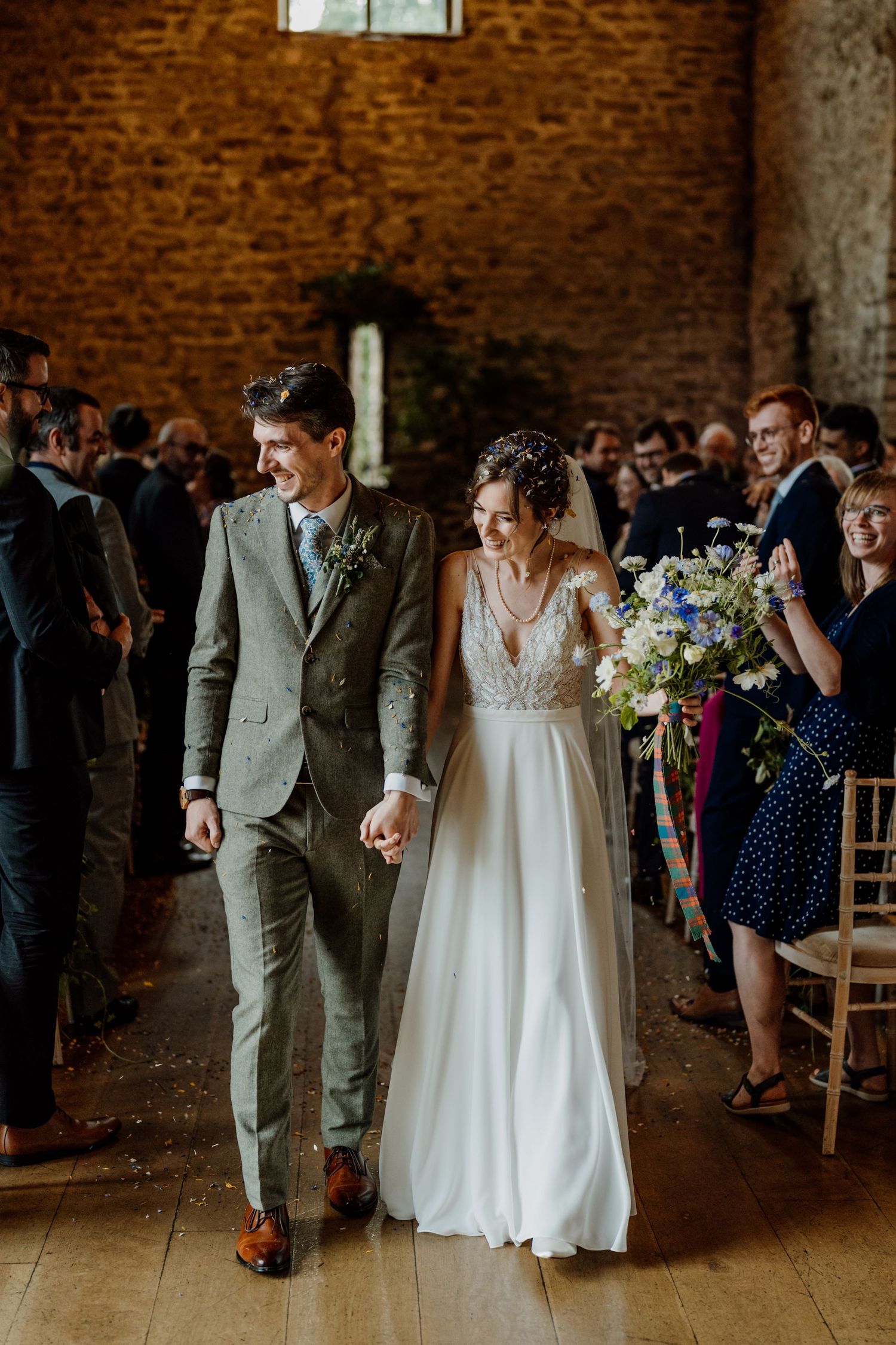A couple walks down the aisle in a rustic brick venue with natural lighting.