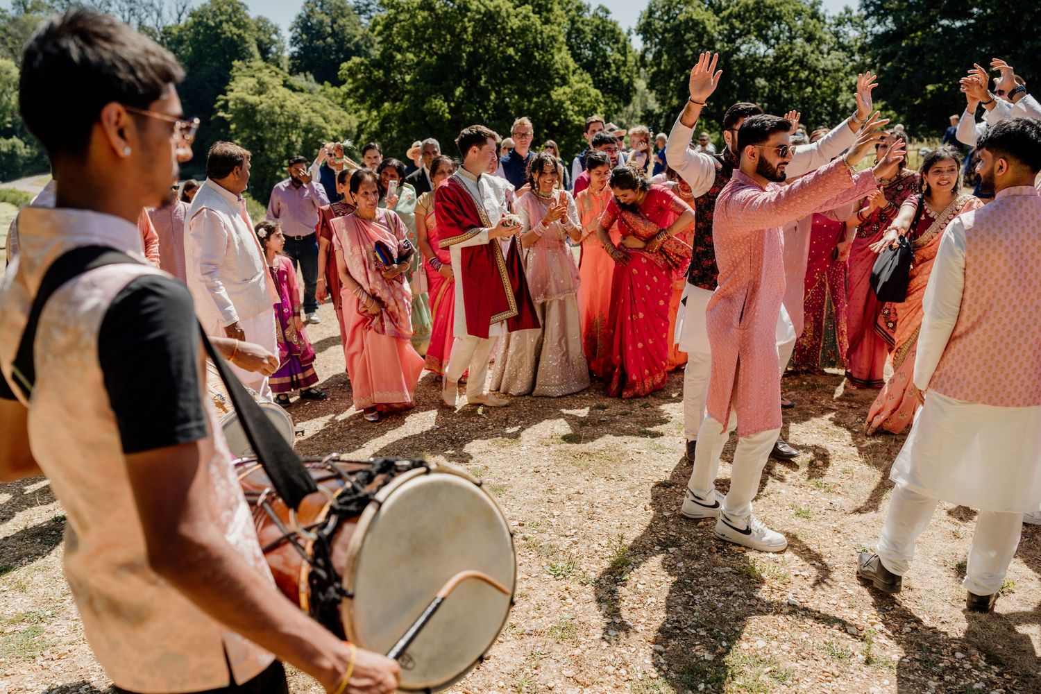 A festive outdoor celebration with people in red and white attire dancing and playing drums on a sunny day.
