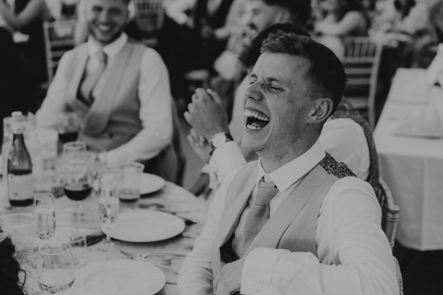 Black and white photo of wedding guests laughing during reception dinner.