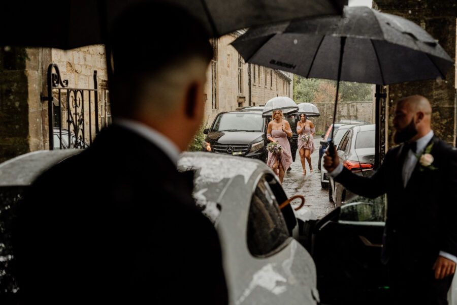 Wedding ceremony guests sheltering under black umbrellas on a rainy day.
