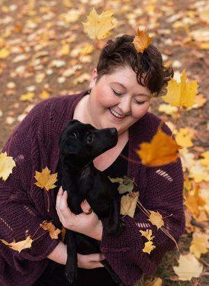 Woman playing in a leaf pile with a small black dog.