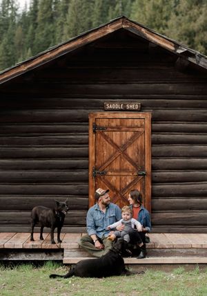 Couple in front of rustic cabin with their two dogs.