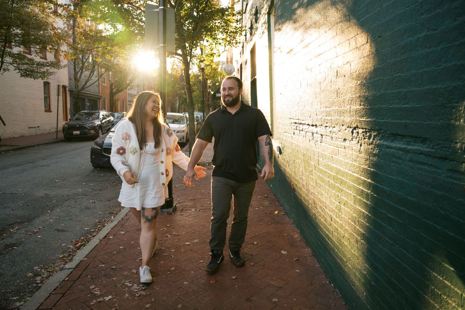 Two people walk together on an urban sidewalk at sunset with golden sunlight streaming through trees nearby.