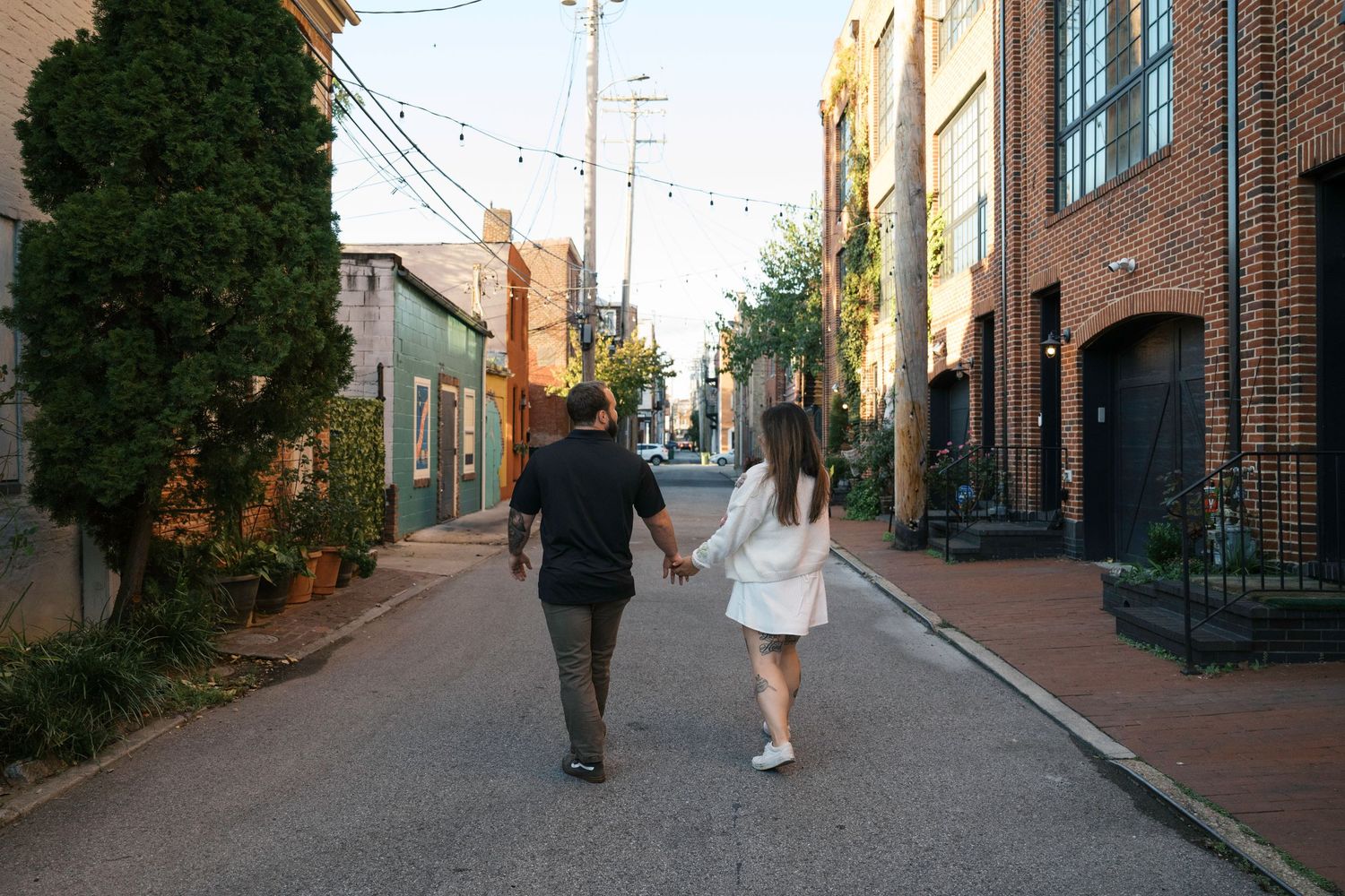 Two people walking down a quiet brick-lined street in an urban neighborhood during sunset.