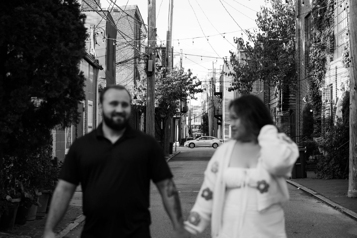 Two people conversing while walking down a residential street with power lines and buildings visible.