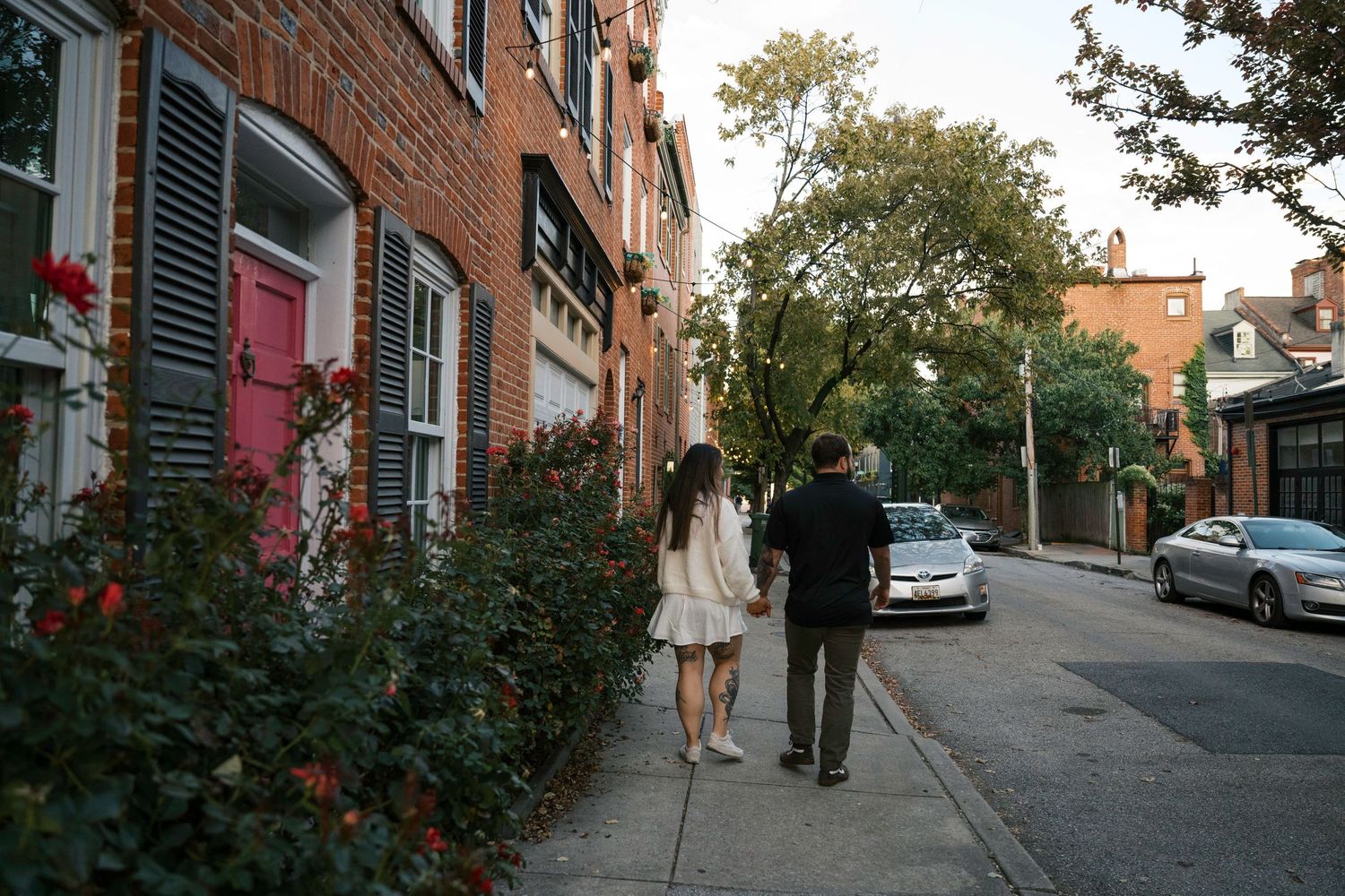 A quiet cobblestone street lined with traditional brick townhouses and parked vehicles in an urban neighborhood.