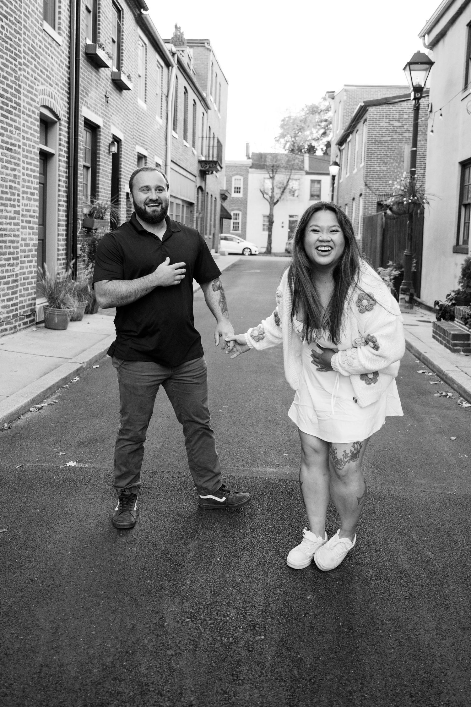 A couple shares a playful moment together on a charming brick-lined street with historic buildings and a lamppost.