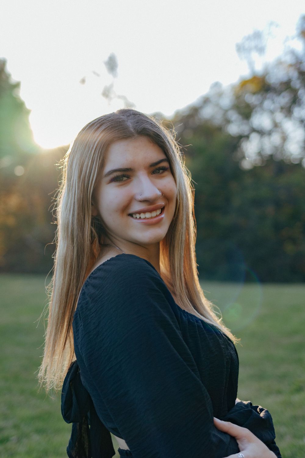 A person in a black sweater poses playfully in a grassy field during golden hour.