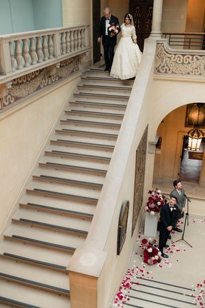 A bride is escorted down a staircase during a wedding ceremony at Cuneo Mansion.