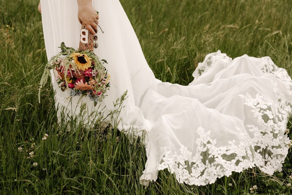 A white wedding dress train with delicate lace details trails across lush green grass in an outdoor setting.