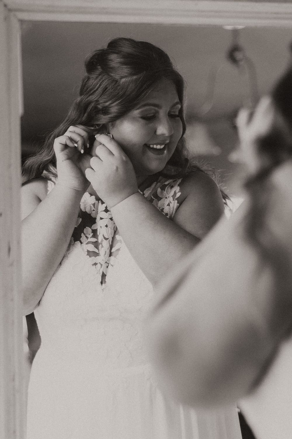 Black and white sequence showing bride getting ready and adjusting her hair while smiling in a floral dress.