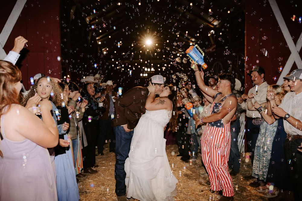 Wedding guests dance and celebrate on a dimly lit dance floor with confetti falling from above during a reception.
