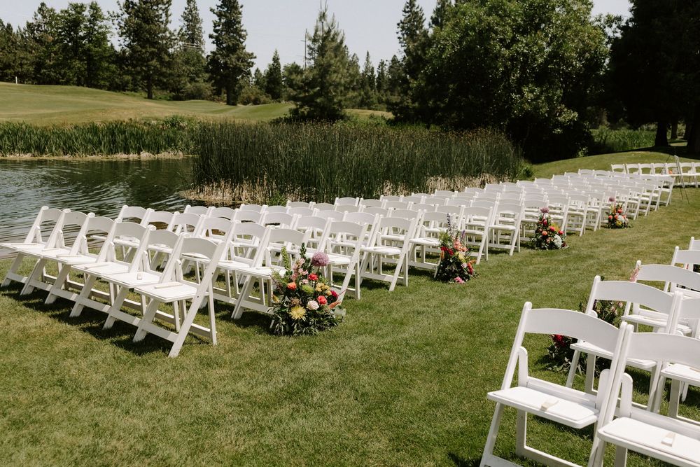 White folding chairs arranged in rows on a lush green lawn near a pond for an outdoor wedding ceremony.