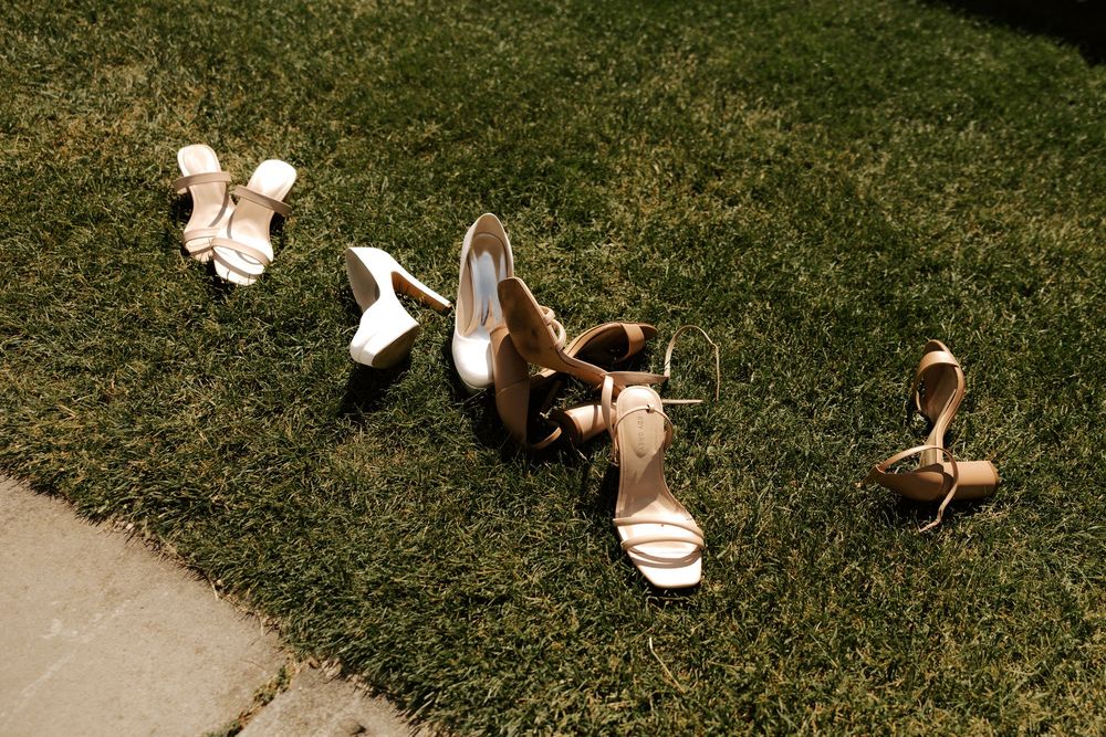 Collection of elegant beige and white wedding shoes arranged on green grass in sunlight.