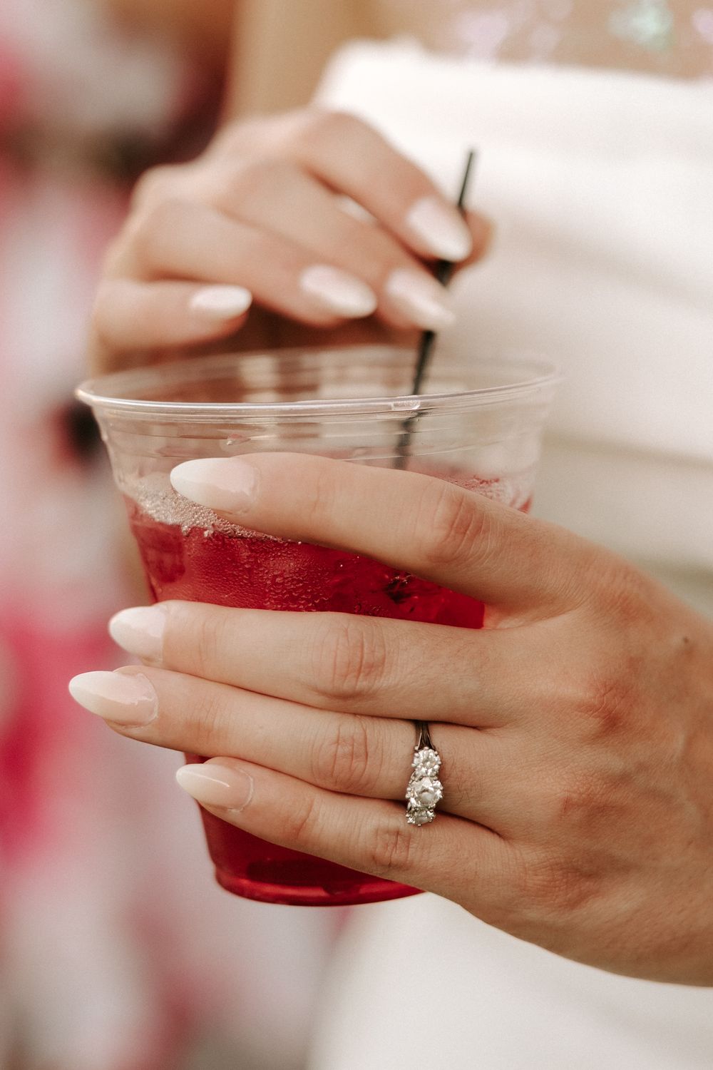 Hand holding a red drink in a clear glass, showing off an elegant diamond engagement ring.