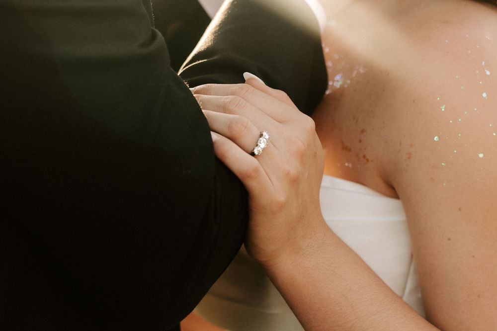 A close-up view of a hand wearing a sparkling diamond engagement ring in natural lighting.