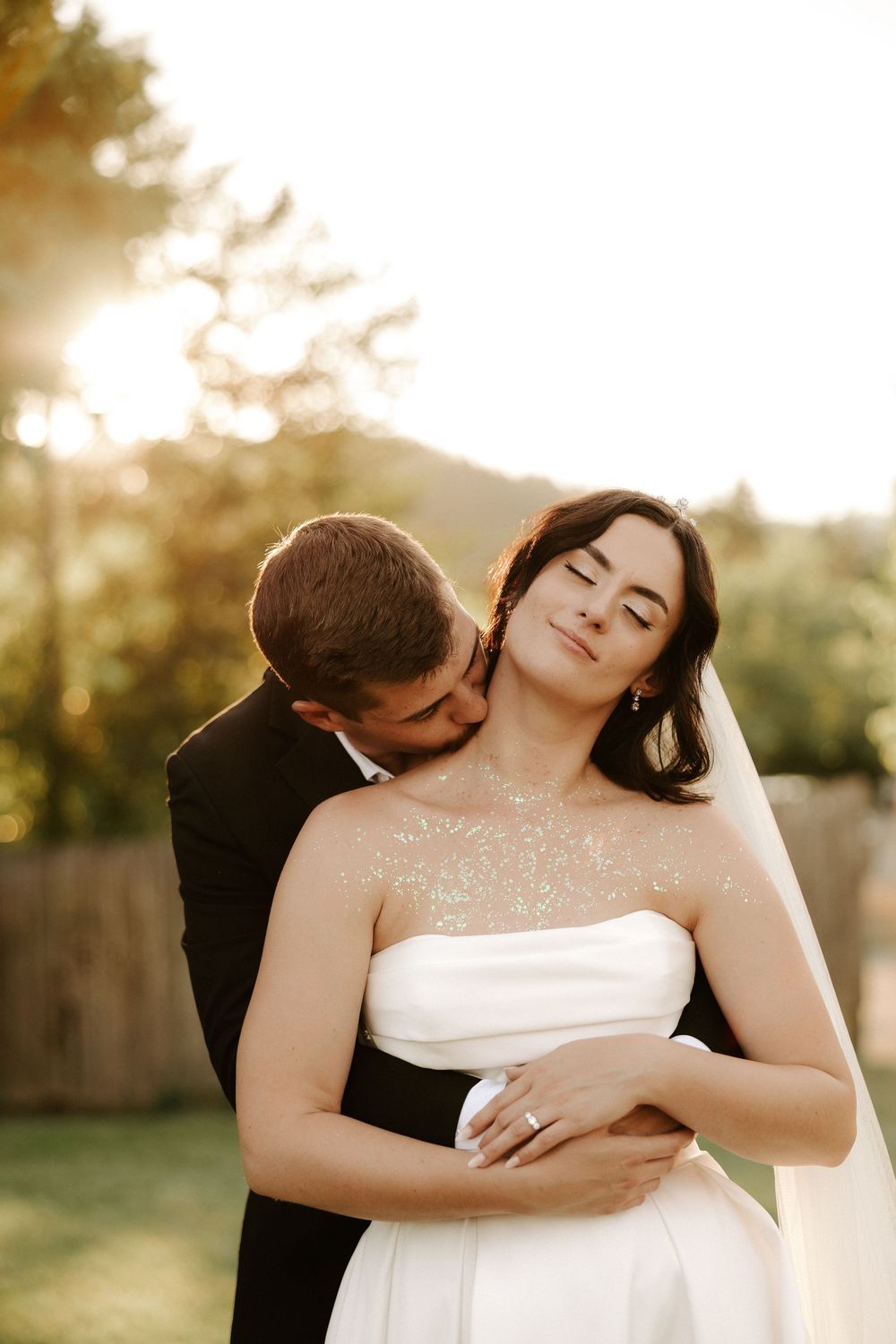 A romantic wedding portrait captured during golden hour in a garden with soft sunlight filtering through trees.