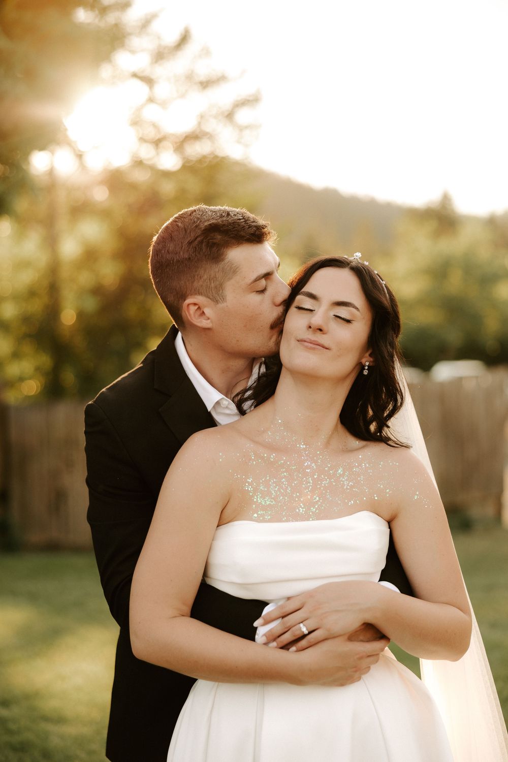 Romantic wedding couple embraces during golden hour sunset in an outdoor garden setting.