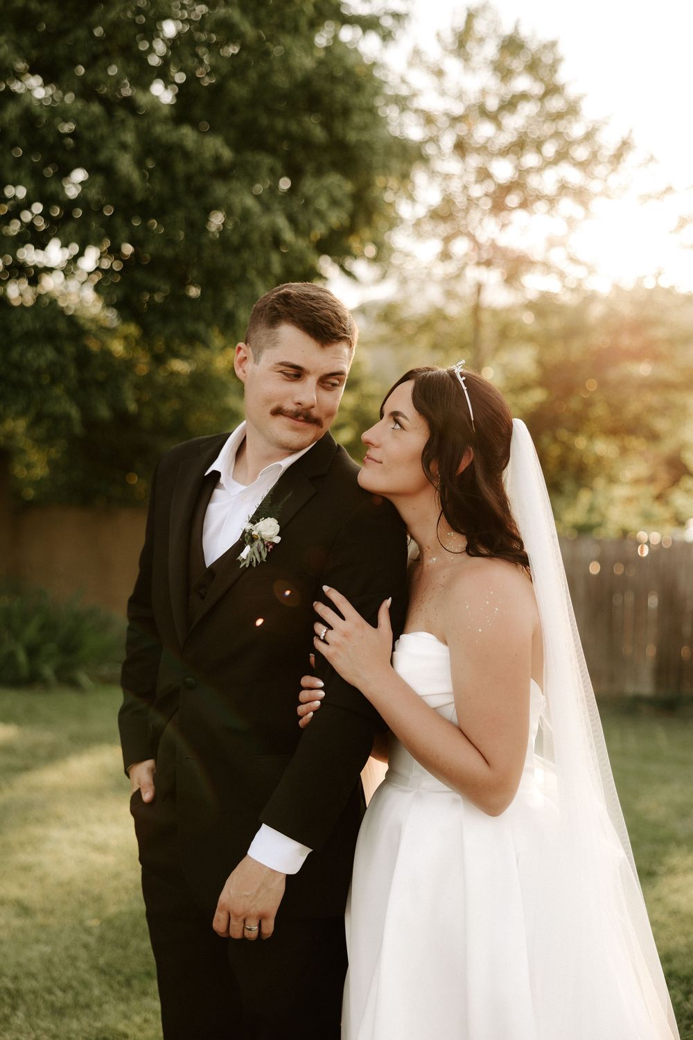 A joyful wedding couple shares an intimate moment while posing in a garden at sunset.
