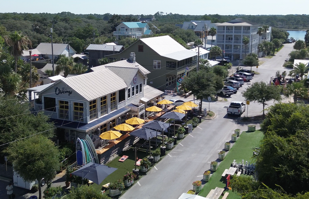 Aerial panoramic view of coastal buildings and yellow school buses parked along winding roads in a seaside community.