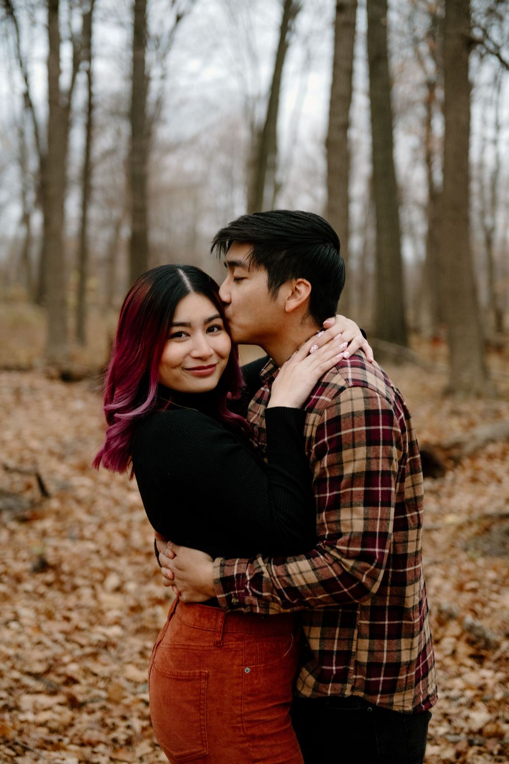 A romantic autumn photoshoot in the woods with a couple wearing plaid and corduroy against fallen leaves.