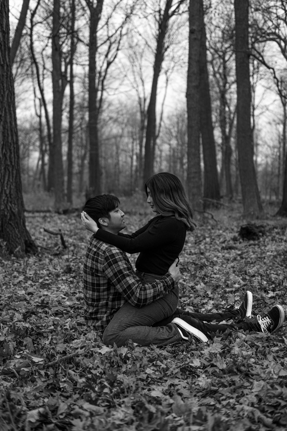 Person lying on autumn leaves in black and white forest scene reading a book in plaid shirt.