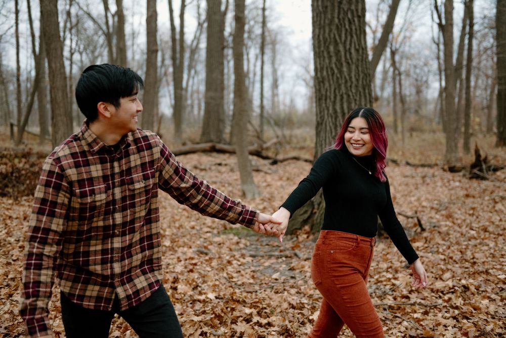 Two people playfully toss autumn leaves in a forest during a fall photo session.