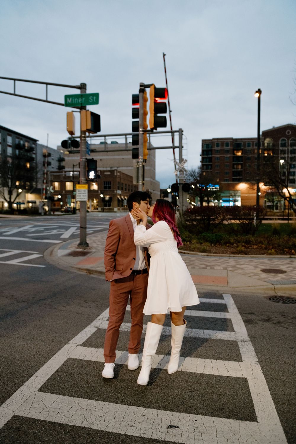 A couple in brown and white outfits walking together at dusk near a street intersection with traffic lights.
