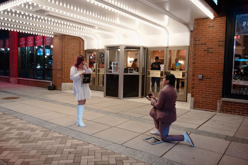 A proposal moment captured outside a shopping center entrance with brick columns and glass doors.