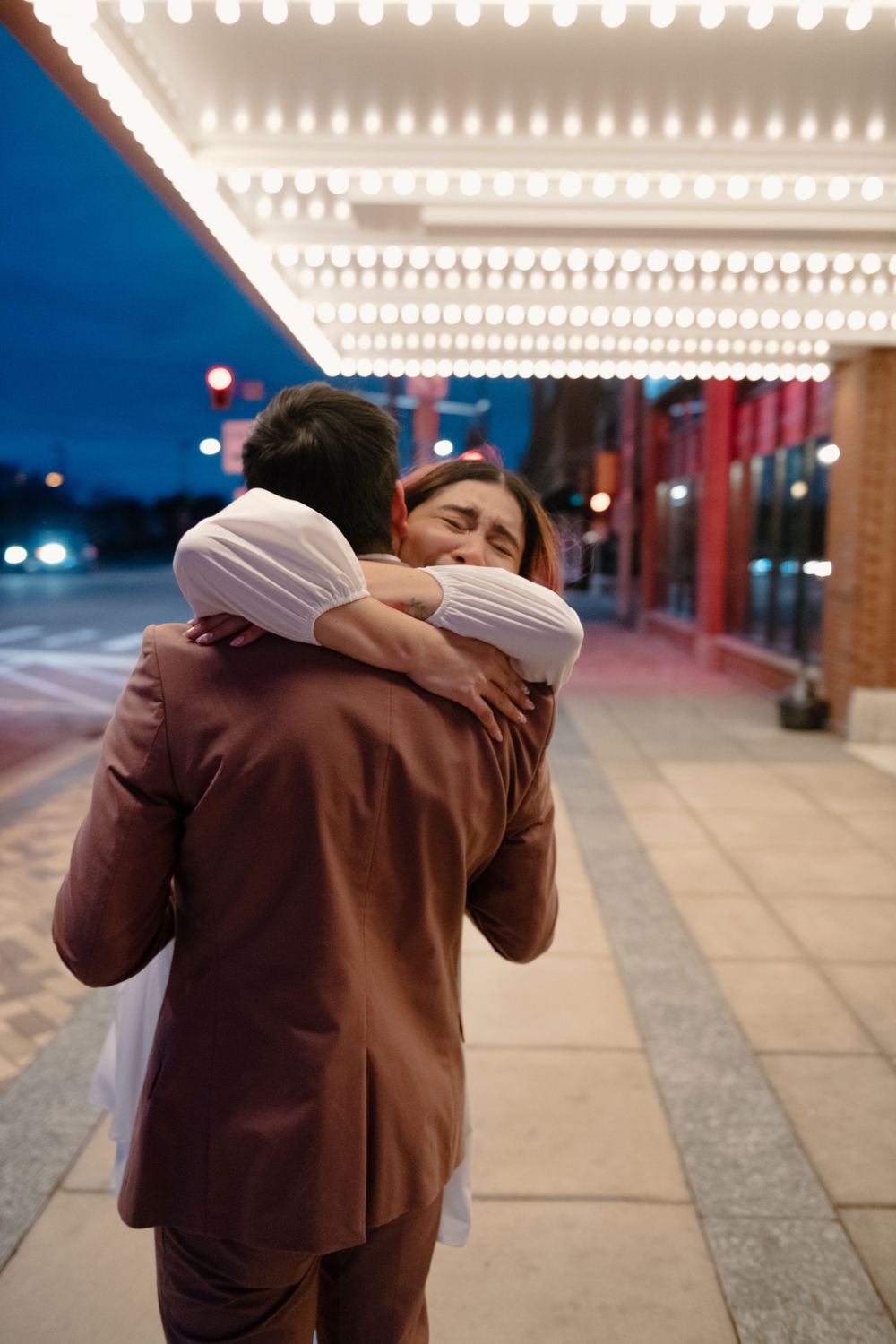 A tender embrace captured under illuminated theater marquee lights at dusk.