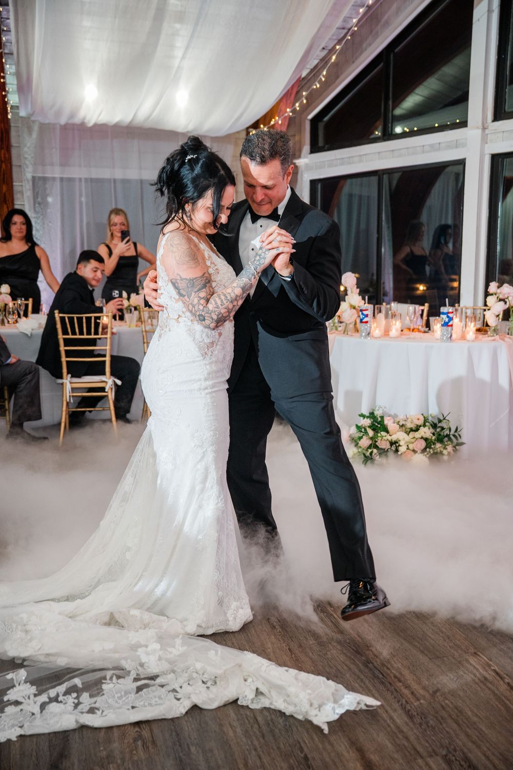 Newlyweds share their first dance surrounded by romantic fog effects on a wooden dance floor at their wedding reception.