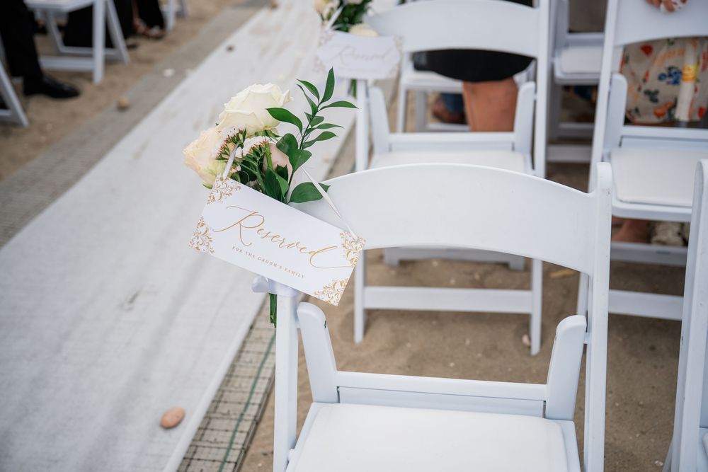 White folding chairs with floral decorations arranged for outdoor beach wedding ceremony.